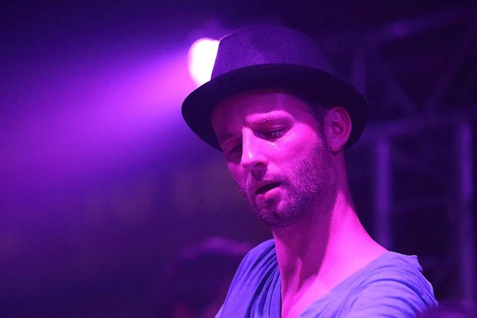 Felix Kröcher mit Hut in Nahaufnahme am Pult, violettes Licht
