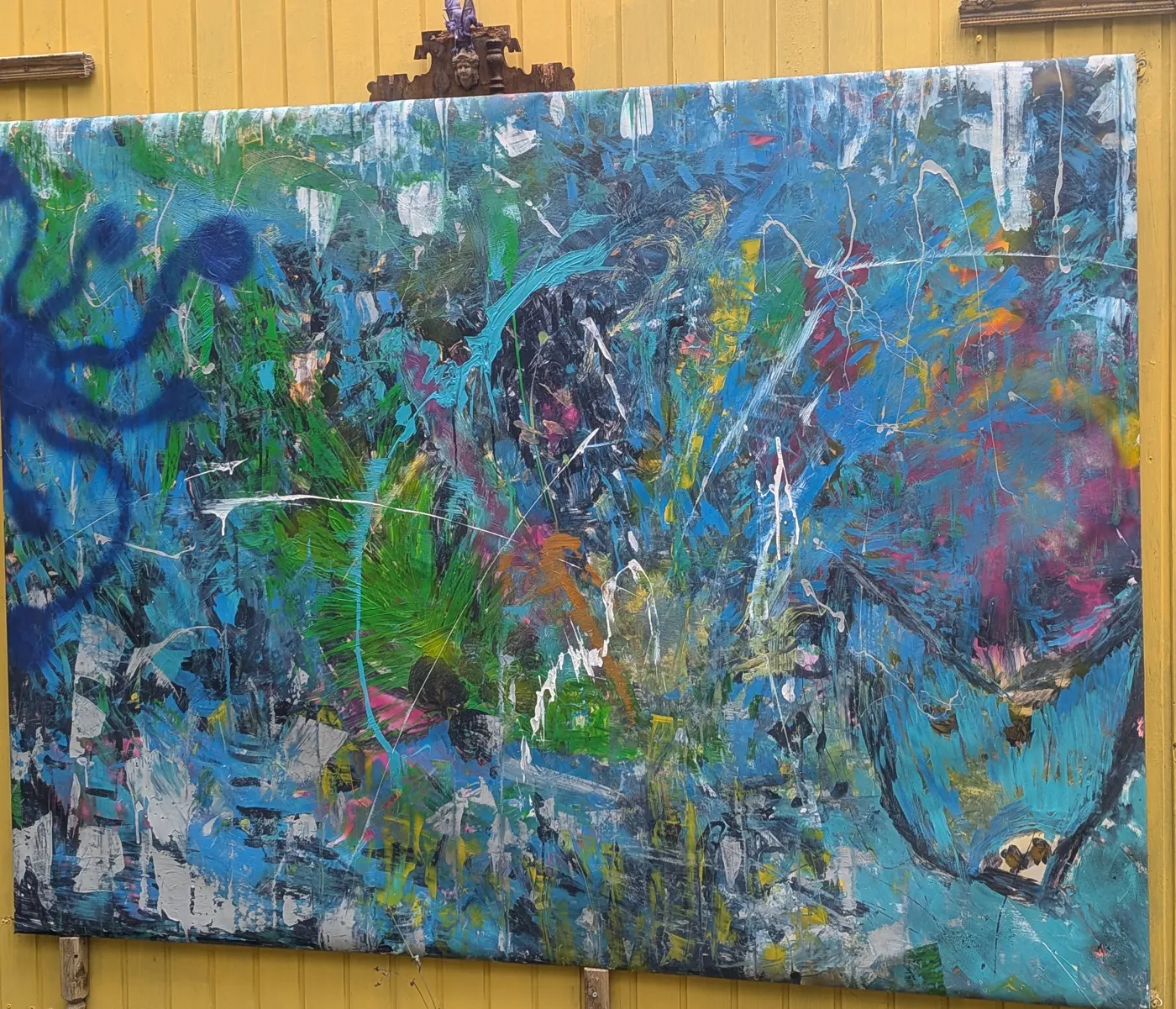 Großes abstraktes Gemälde in Blau und Grün mit weißen, gelben und rosa Farbspritzern, an einer gelben Holzwand