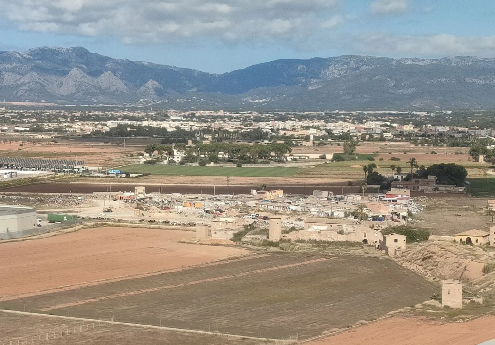 Luftbild: die Siedlung Son Banya mit flachen Bauten zwischen Feldern, dahinter Palmas Umland und die Serra de Tramuntana